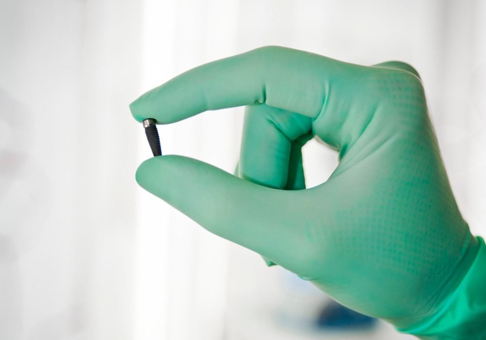 Hand with gloves holding a dental implant